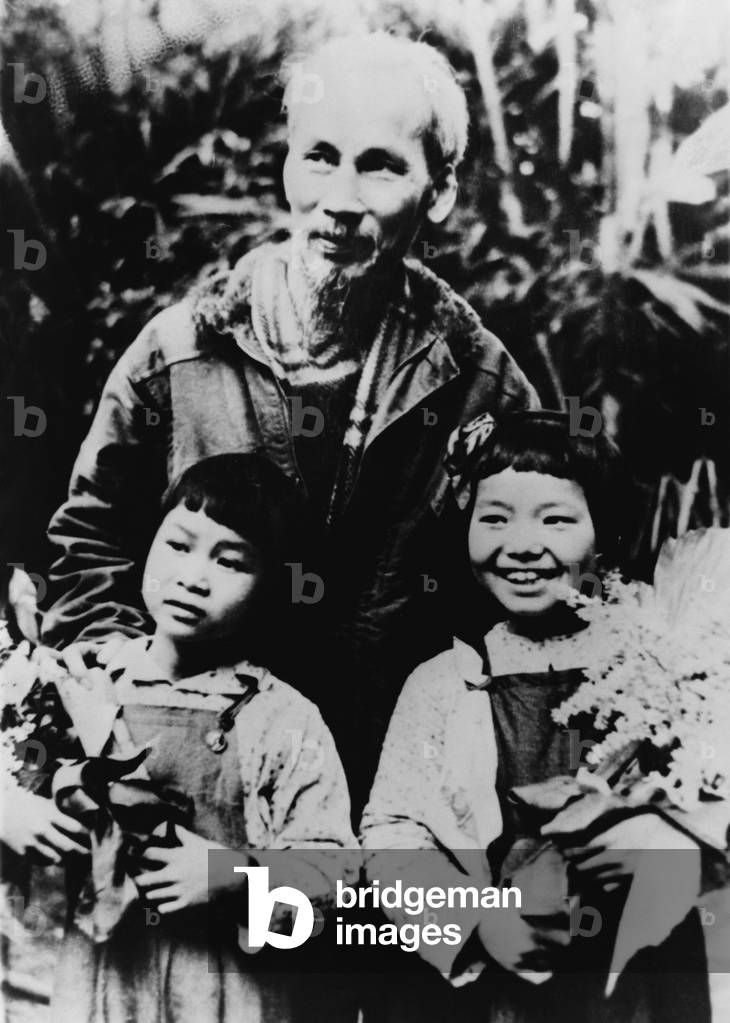 Ho Chi Minh (1890-1969), North Vietnamese leader revolutionary with his arms on the shoulders of two young girls. c. 1954
