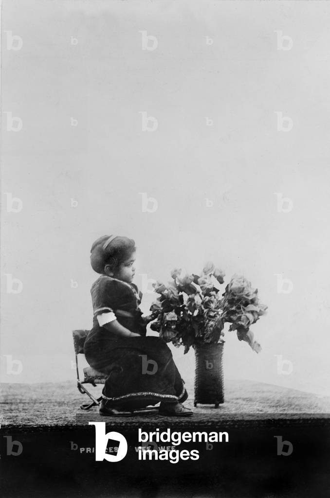 Princess Wee Wee, African American dwarf, full-length portrait, seated, facing right, with bouquet of flowers, 1915