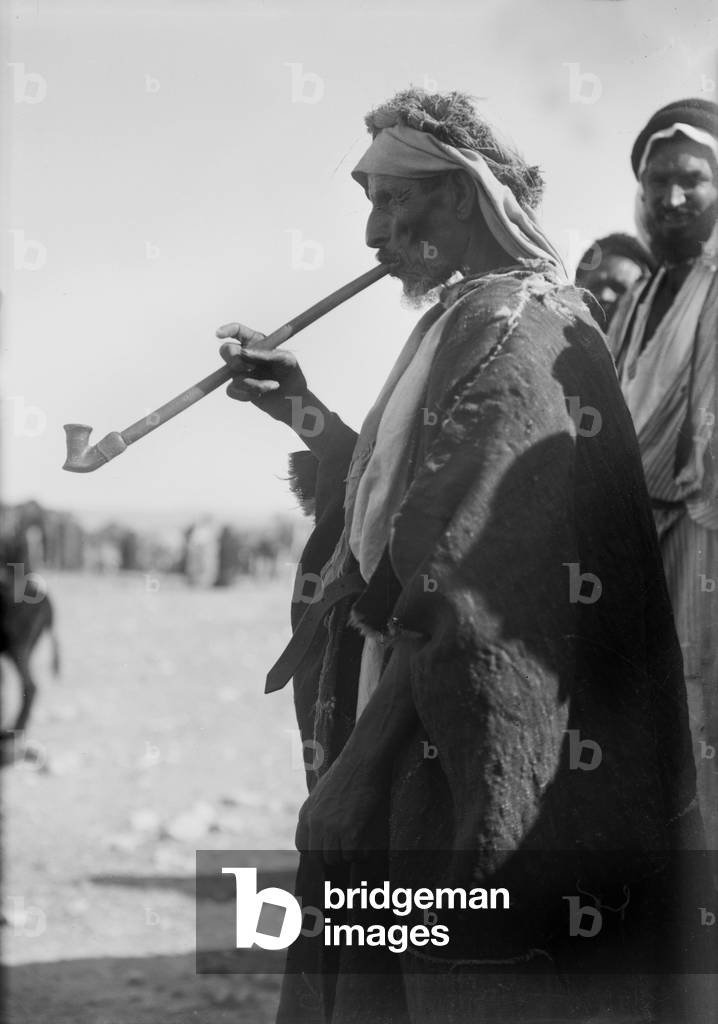 Bedouin man smoking a long pipe., photograph 1920