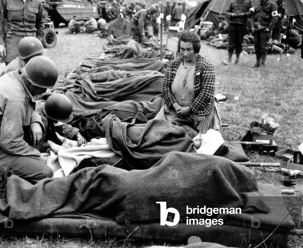 Three U.S. Army medics attend to a young girl's injury on Aug. 1, 1944, in Normandy. She was probably wounded during Operation Cobra, the U.S. Offensive against German troops in the Falaise Pocket. Other stretchers bear wounded soldiers. France, World War 2
