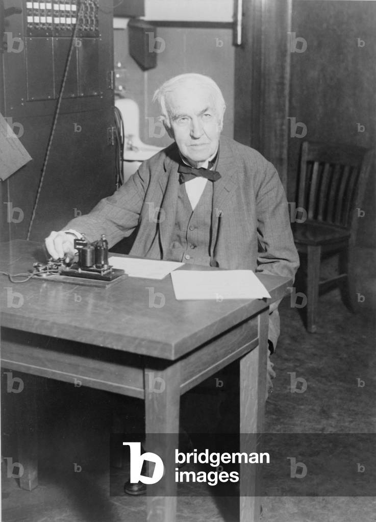 Thomas Edison, seated at desk, demonstrating an old telegraph transmitter in his West Orange, New Jersey, laboratory, 1930