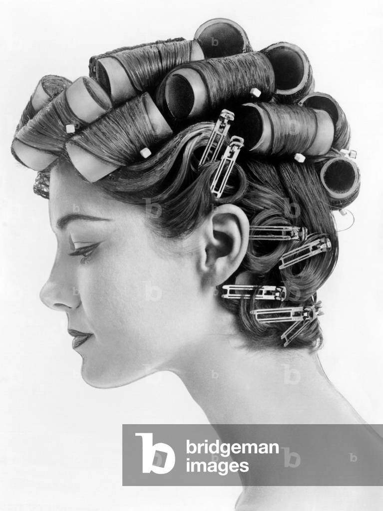 1960s bouffant hair styles were created with big rollers on top of the head and pin curls to create a soft flip up at the neck. Profile view. June 25, 1962