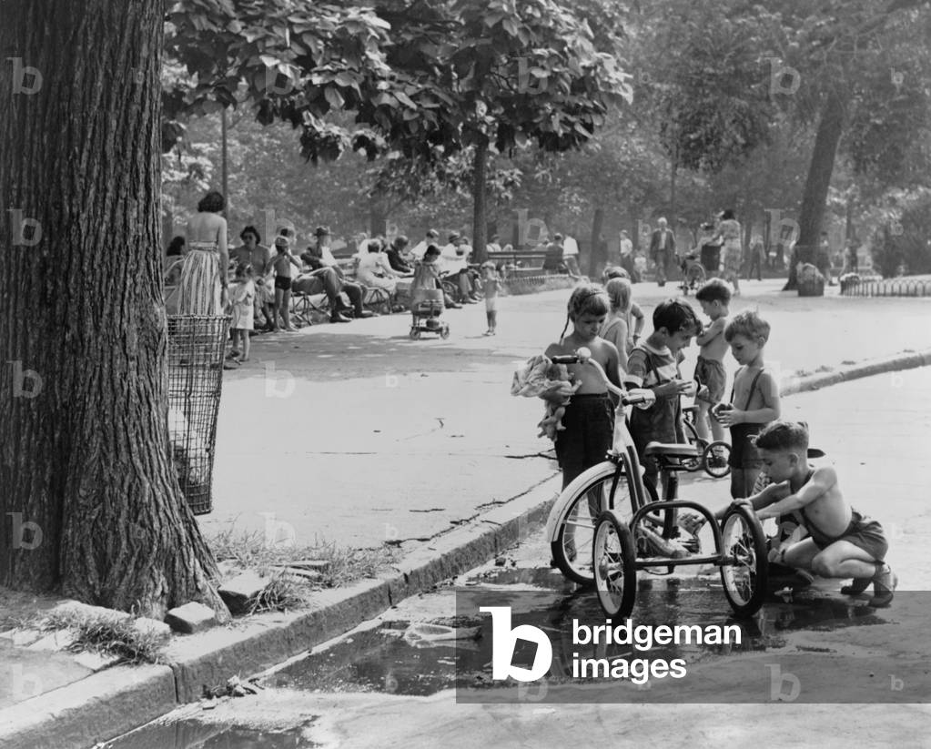 Children with tricycles play near a puddle in Washington Square Park. New York City Aug. 3, 1948