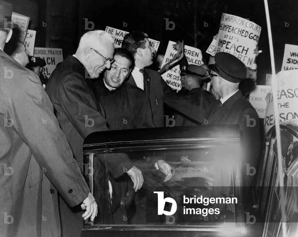 Chief Justice Earl Warren is escorted through crowd of protestors carrying placards attacking the Supreme Court's 1963 ruling (Abington School District v. Schempp) to prohibit prayer in U.S. public schools