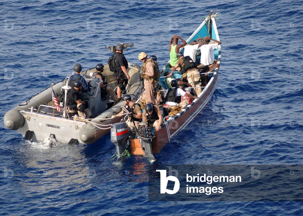 U.S. Navy sailor inspects the outboard engines on a skiff suspected of participating in recent pirate activity while fellow sailors board search and question men on ship. May 31 2010 in the Gulf of Aden., Photo by:Everett Collection