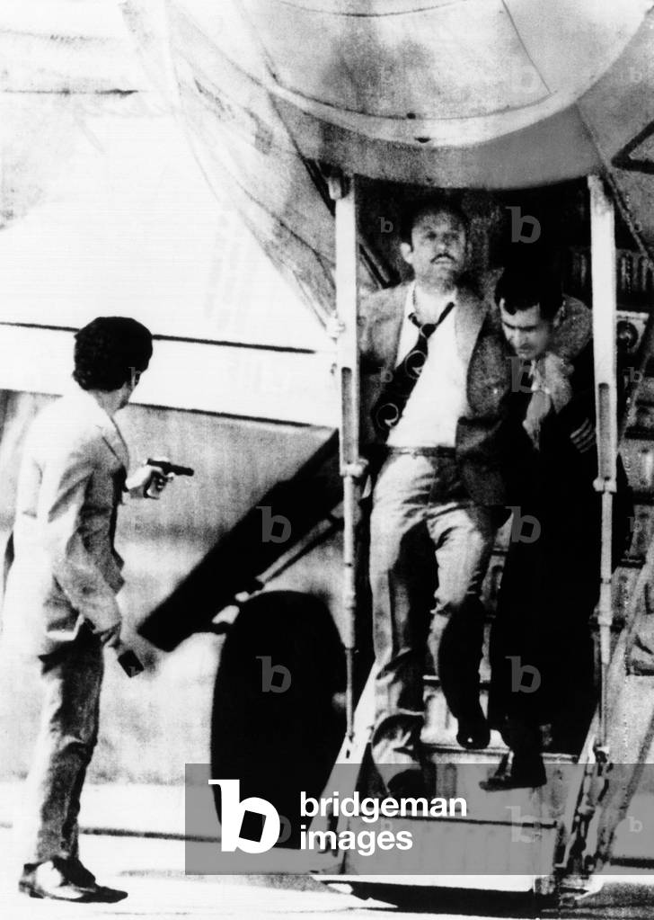 An armed hijacker (left) watches as Turkish Airlines crew member employee assists a passenger who suffered a heart attack on the air liner at Sofia, Bulgaria. Members of the People's Liberation Army of Turkey threatened to blow up the plane and its passengers unless Turkey freed three guerrillas condemned to death. May 3, 1972