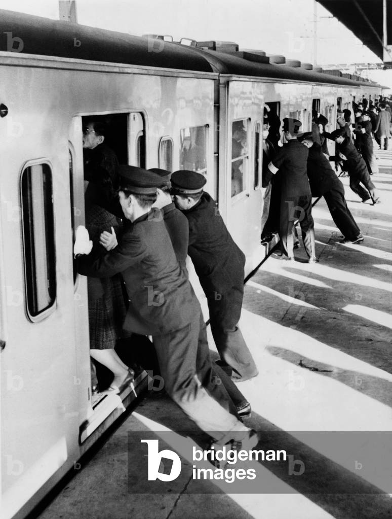 Japanese college students employed as uniformed 'pushers' cramming Tokyo commuters into railroad passenger cars. 1962