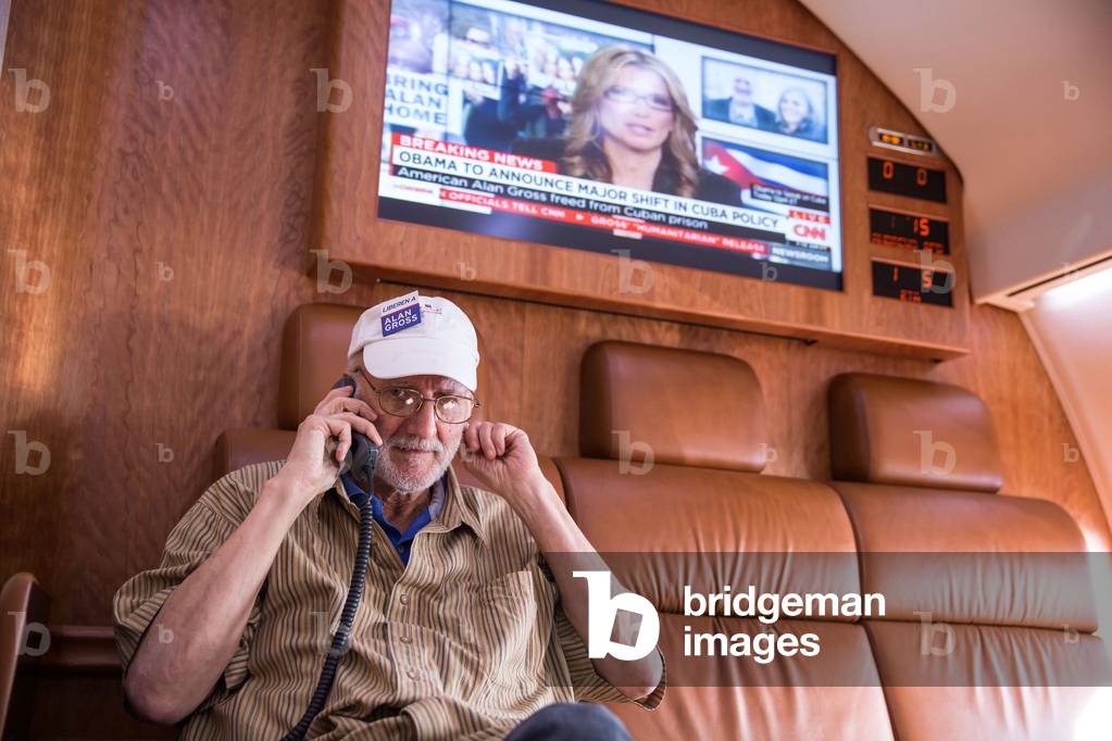 President Barack Obama talks on the phone with Alan Gross after his release from a Cuban prison. Above a television news headline reads, 'Obama to Announce Major Shift in Cuba Policy.' After five years in prison, Gross was onboard a government plane flying from Cuba to Andrews Air Force Base, Md., Dec. 17, 2014