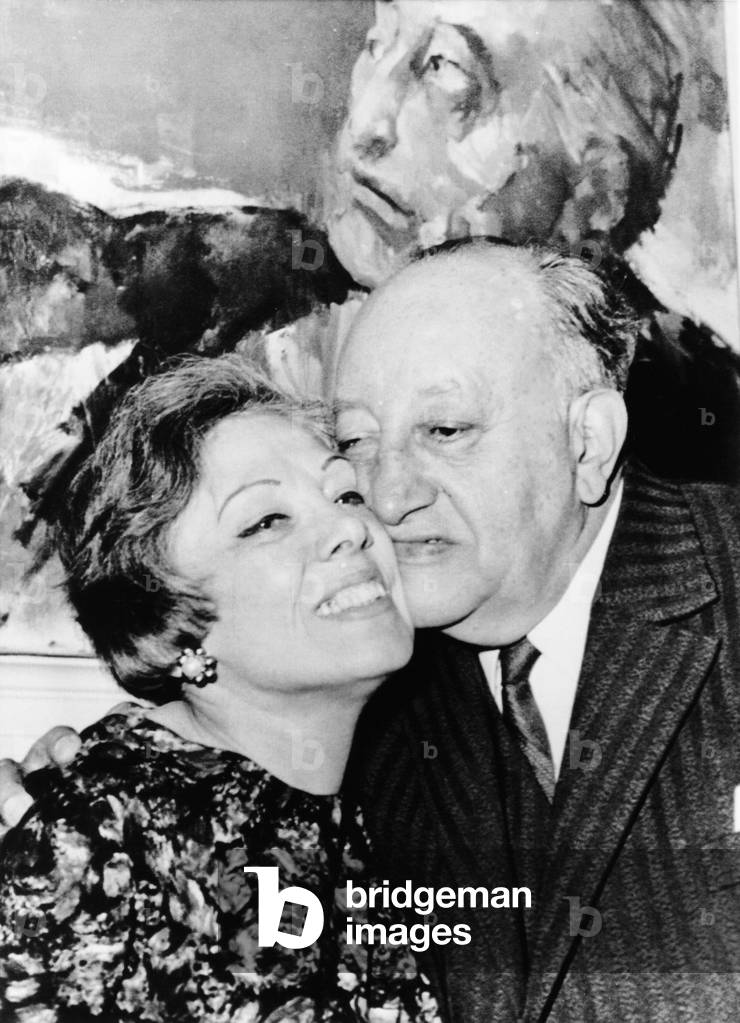 Guatemalan poet Miguel Angel Asturia with his wife Blanca Nora y Arau de Asturias. The author was cited for his highly colored writing rooted in a national identity and Indian traditions. They pose in front of an expressionist portrait of Asturias. Oct. 1967