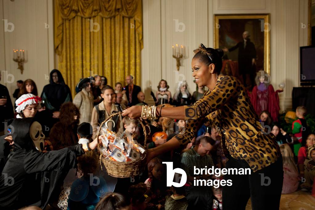 First Lady Michelle Obama hands out treats during a Halloween reception for military families and children of White House staff in the East Room of the White House. Michelle wears a leopard print sweater set with black slacks and gold bangle bracelets. Oct. 31 2009.,