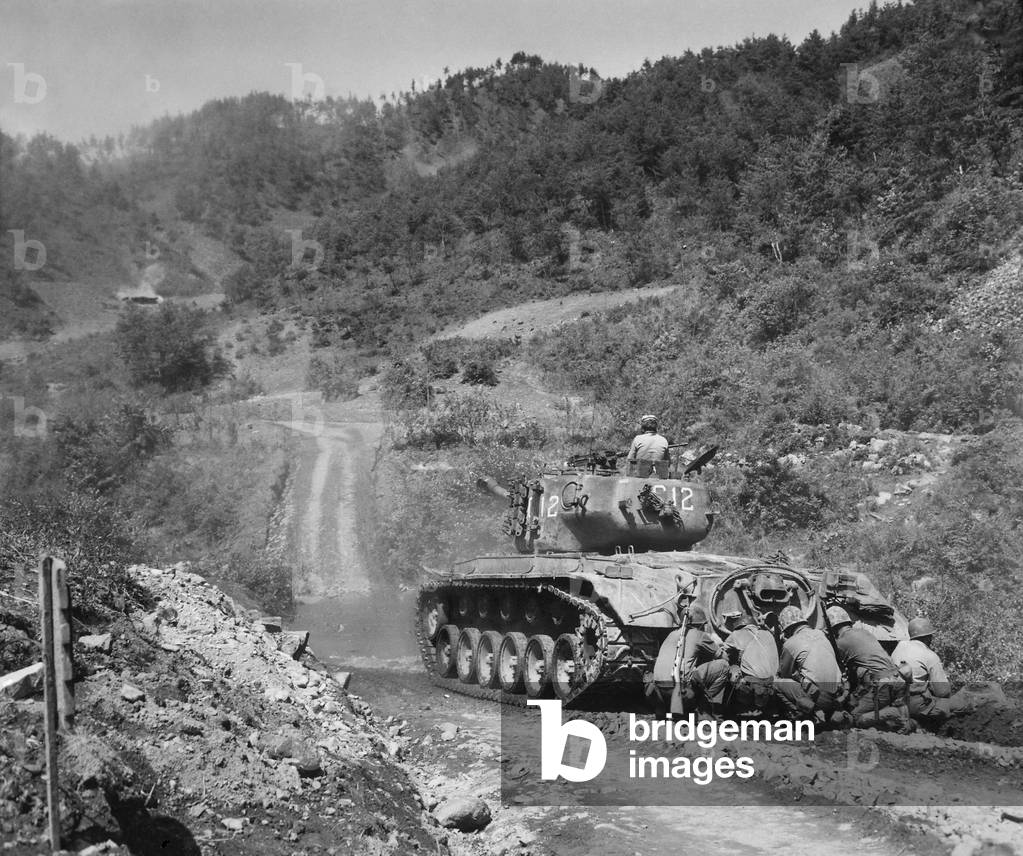 U.S. Marine infantrymen take cover behind a tank while it fires on Communist troops ahead. Hongchon Area, Central Korea, May 22, 1951. Korean War, 1950-53