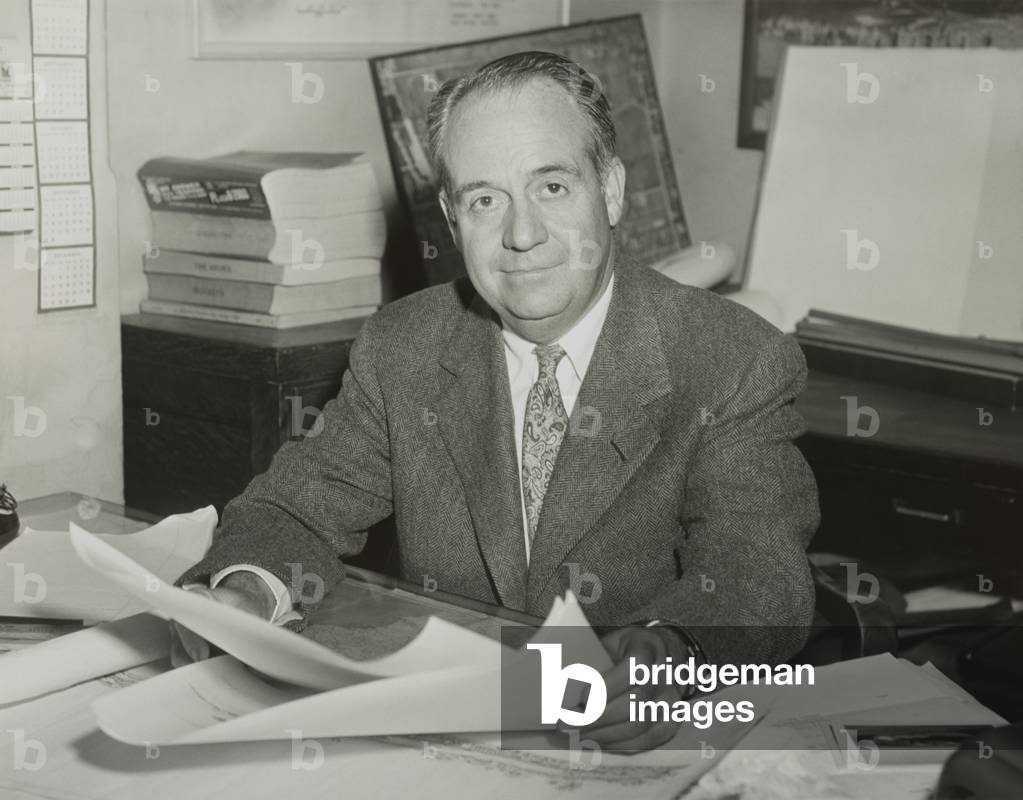 Robert Trent Jones, golf course architect, sitting at desk and holding drawings in 1953.