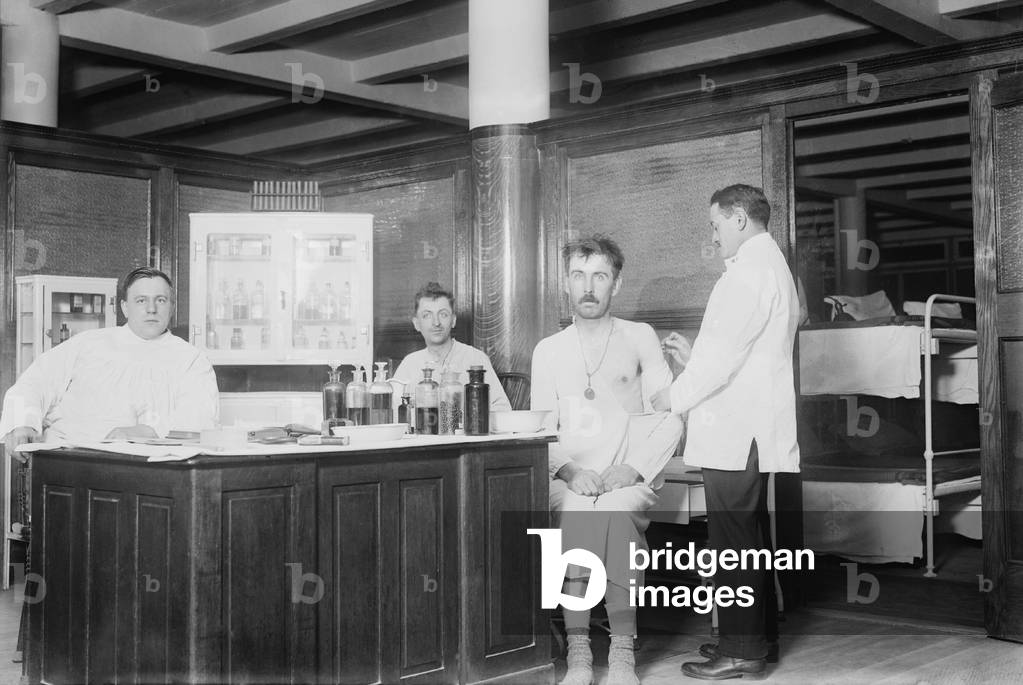 Two recently bathed men are given vaccinations by the doctor at New York City's Municipal Lodging House. c. 1910