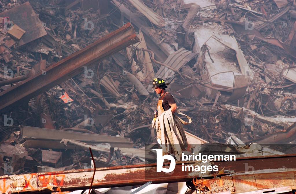 Fire fighter carries a fire hose over smouldering fires and wreckage at Ground Zero, Sept. 18, 2001 (photo)
