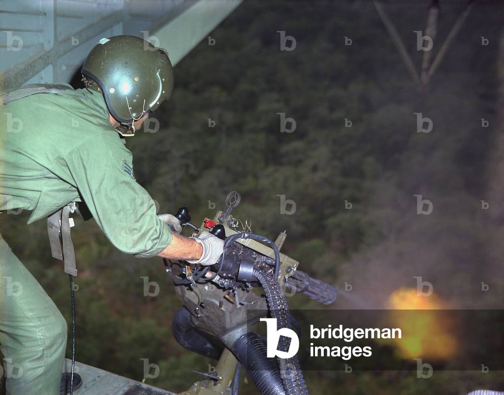 Vietnam War. US Air Force helicopter door gunner fires a mini-gun during a rescue patrol over South Vietnam. Oct. 10, 1968