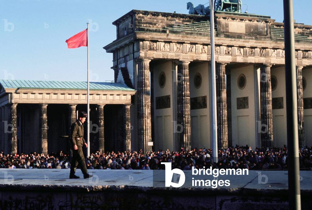Crowds of Berliners around the Brandenburg Gate following the structure's official opening on Dec. 22 1989. In the foreground an East German guard walks on the Berlin Wall