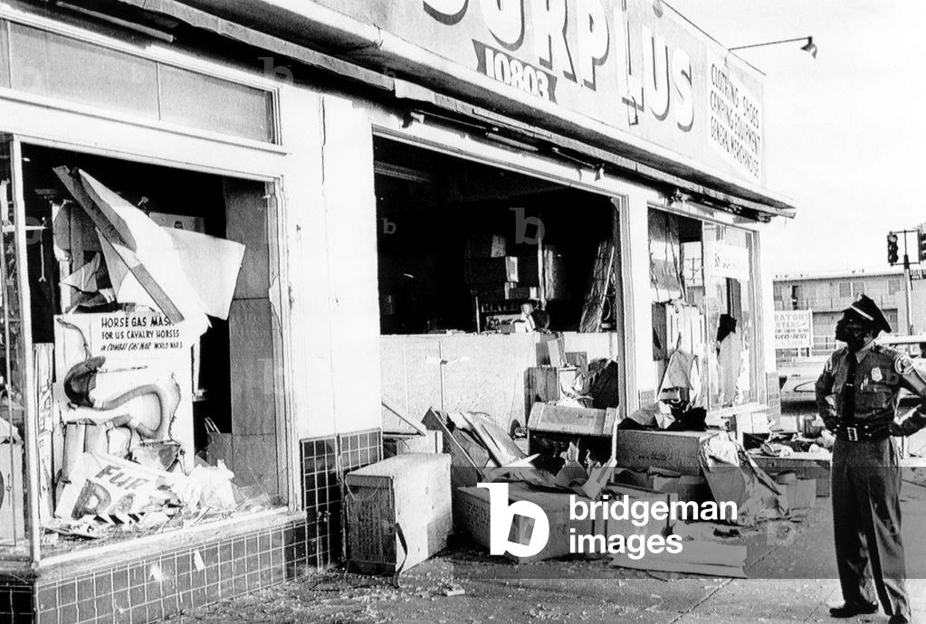 A police officer inspects the damage after the riot in Watts, 1965
