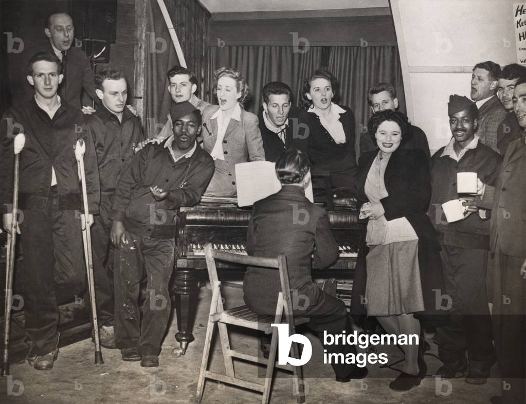 American GIs are entertained by pianist Horatio Davies, at a military hospital in West England. Both black and white soldiers are included in the British ENSA (Entertainments National Service Association) songfest. 1944. World War 2