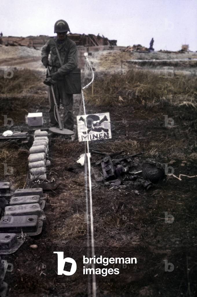 Debarquement de Normandie : Utah beach: U.S. Army Engineer using a mine detector on Utah Beach. Areas outlined with white tape and enemy signs marked dangerous uncleared areas. June 6-10, 1944. Normandy, France, World War 2. B&W Photo with oil color. (JTHIS_2014_3_72)