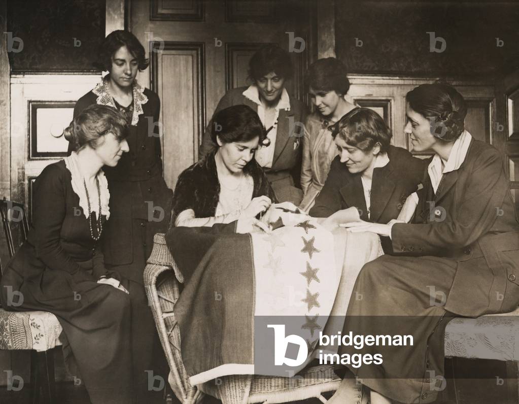 National Woman's Party activists watch Alice Paul sew a star onto the NWP Ratification Flag, representing another state's ratification of the 19th Amendment. Party members, Mabel Vernon is seated far left), and Anita Pollitzer is standing on right. c. 1919