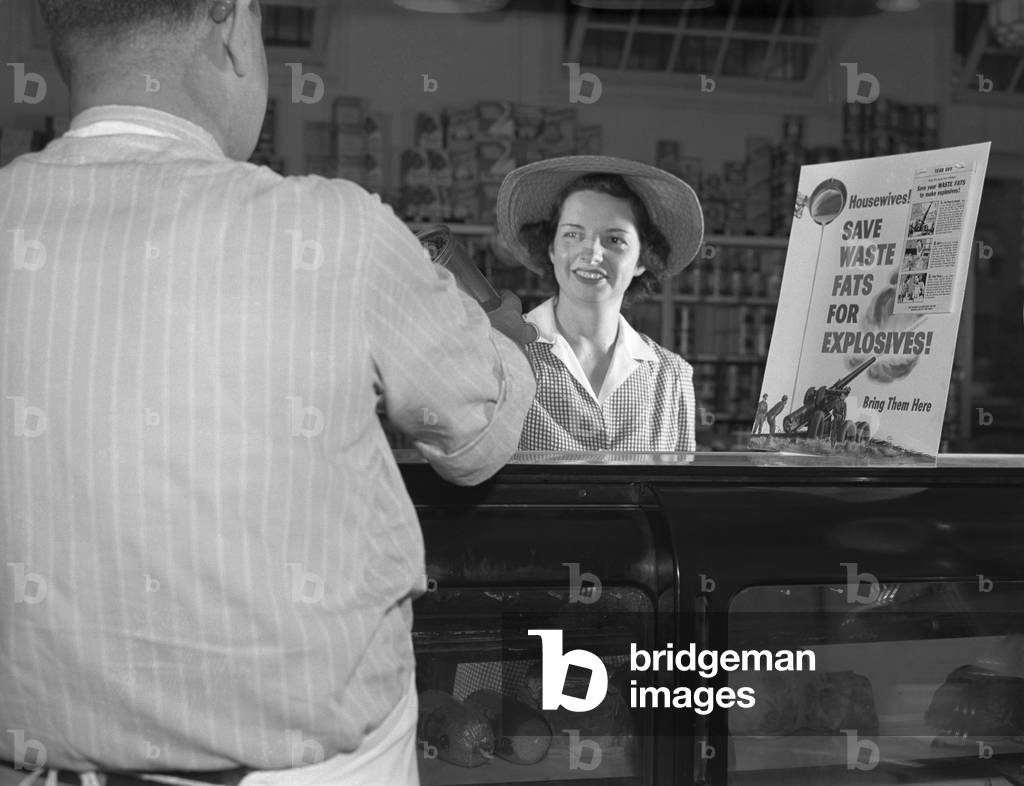 Women at grocery store meat counter. A sign on a grocery store counter reads ' Housewives-Save Waste Fats for Explosives-Bring Them Here'
