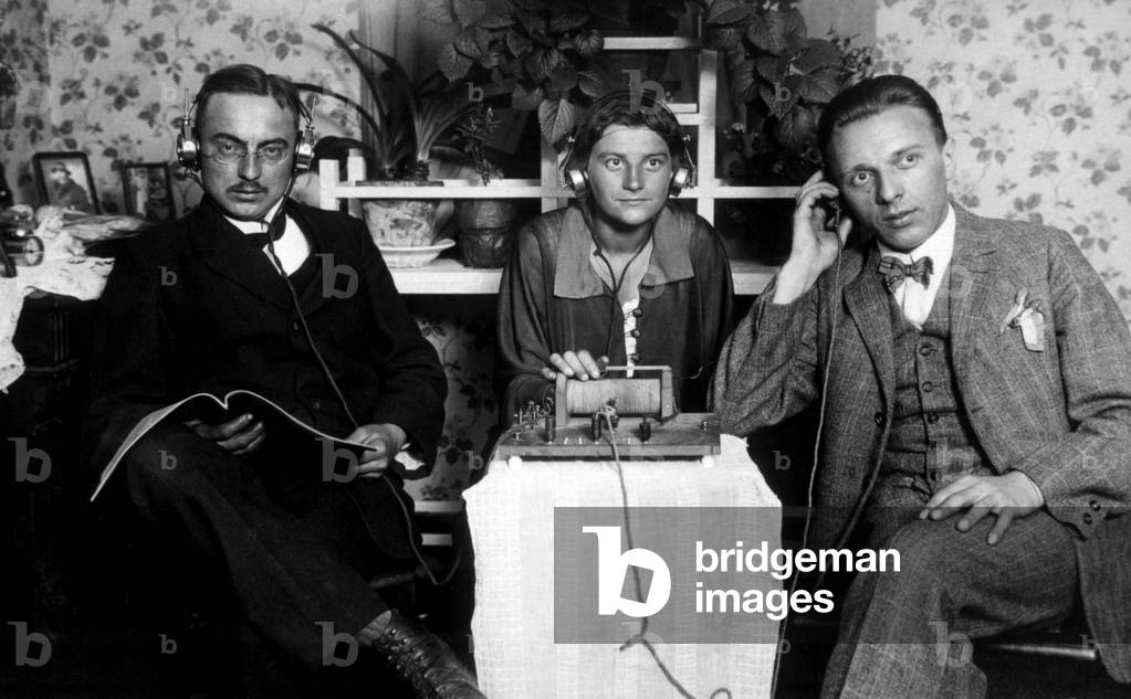 Three people listening to an early radio, c. 1925 (photo)