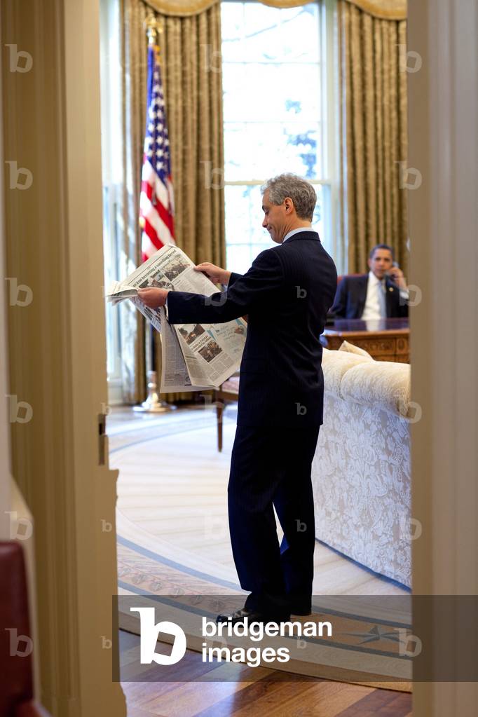Rahm Emanuel looks at a newspaper in the Oval Office as President Obama talks on the phone. April 24 2009. (BSWH_2011_8_107)