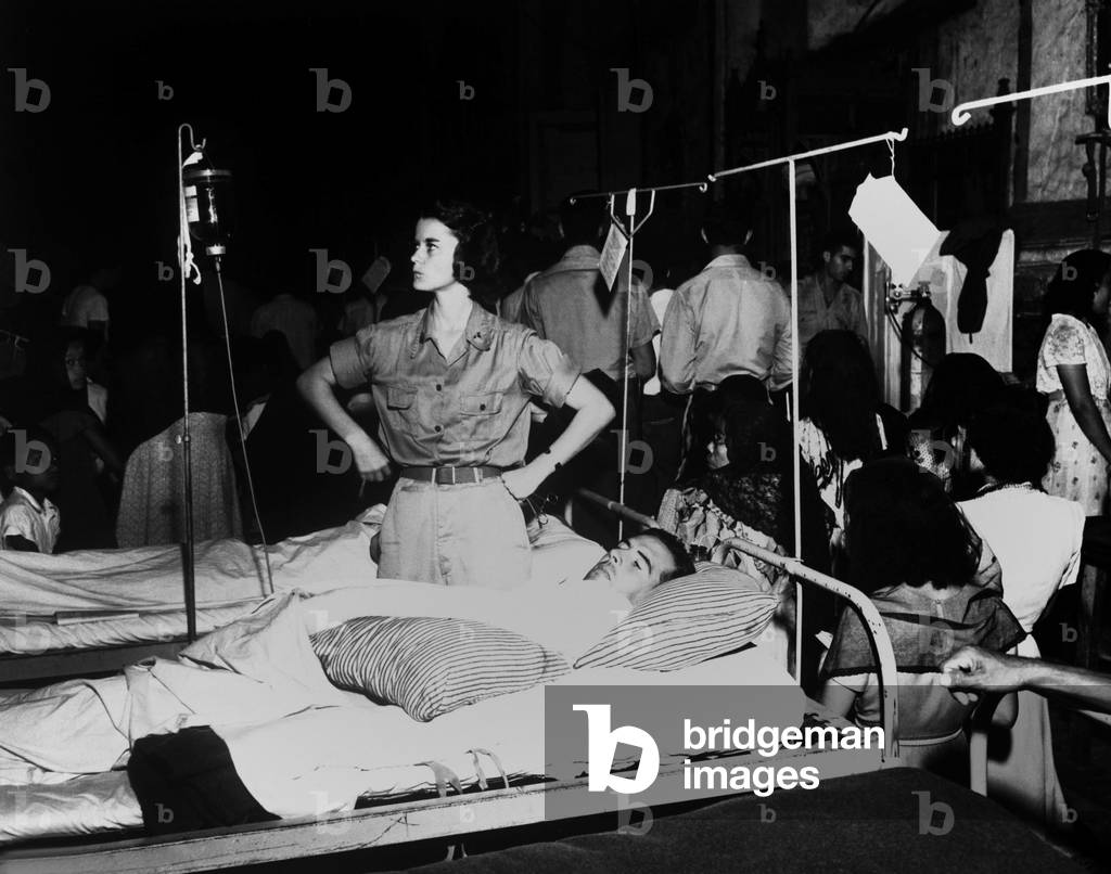Army nurse checks a soldier's glucose drip in the 36th Evacuation Hospital, Leyte, Philippines. The hospital is in the Church of the Transfiguration, and the Filipino congregation attends Christmas Eve services. December 24, 1944. Palo, Philippines, World War 2