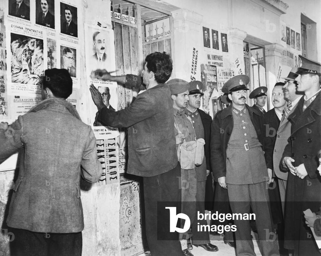 Athens Police and Greek National guardsmen maintain order at the polls in the first free election in ten years. Picture of candidates are posted on the walls of the polling place in the Kolonos District of Athens. March 31, 1946.
