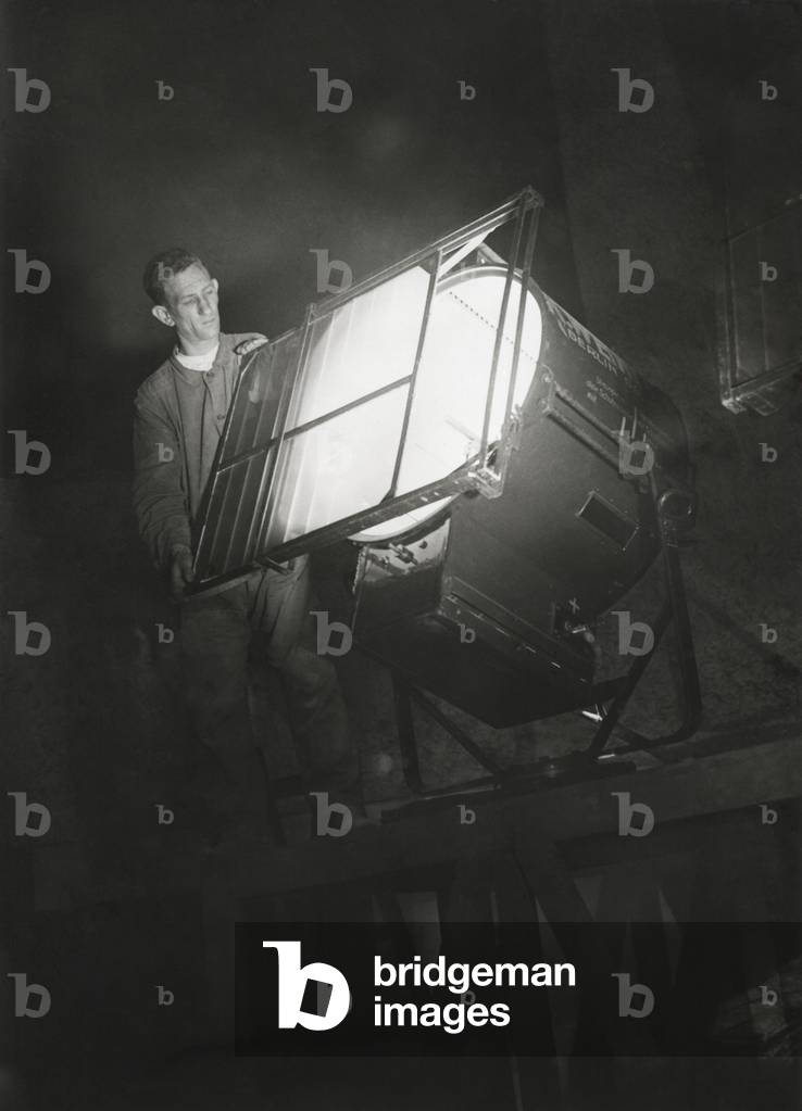 Film engineer using the Dunning Method. He places blue light filter on a special light which will illuminate the filming background. The movie scene was enacted in the studio at a later dates under yellow light. Using dyes and filters, the blue and yellow light could be split apart to create traveling mattes. The Dunning Process was first used in 'King Kong' in 1933.