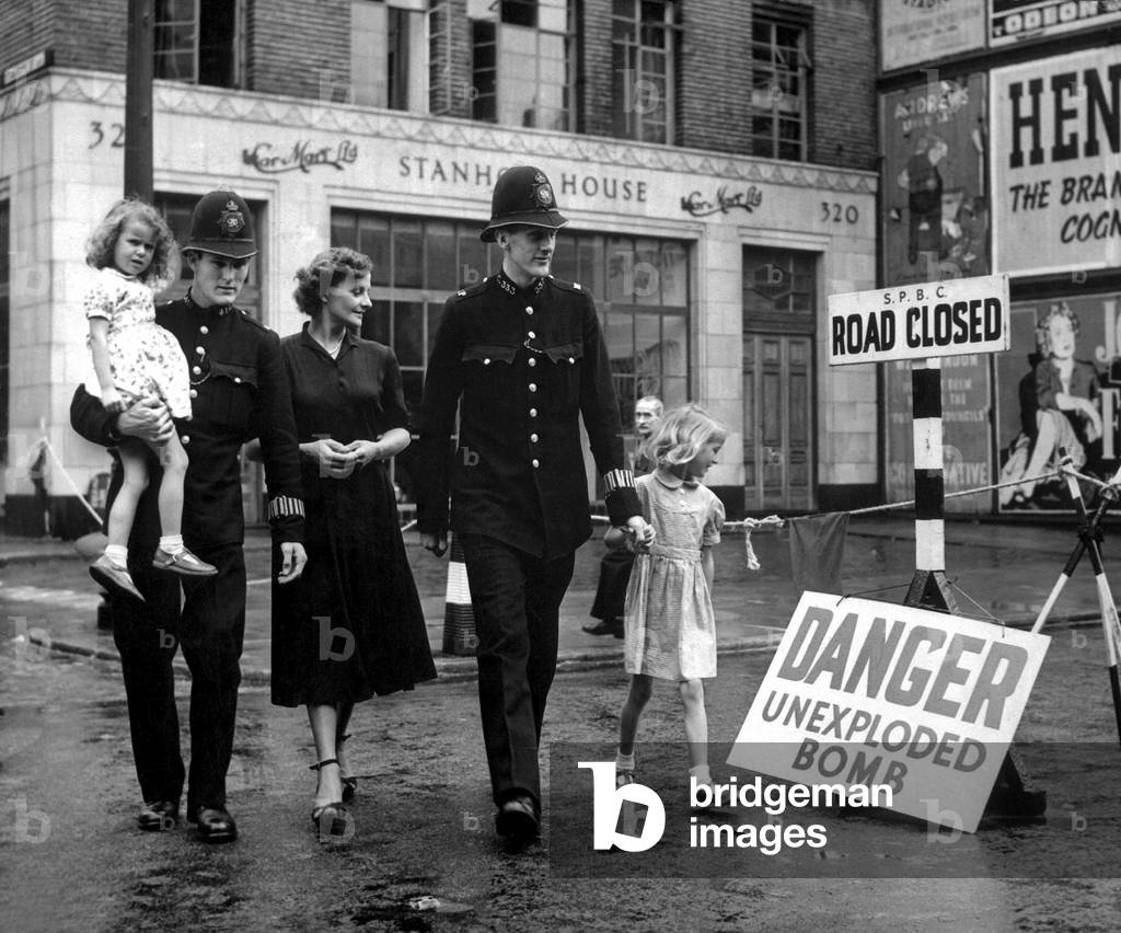 A family is escorted away from the site of an unexploded German bomb in 1948. A 2,500 pound German bomb, buried opposite University College Hospital, London, fell in 1941. After it was defused and removed, residents returned to their homes