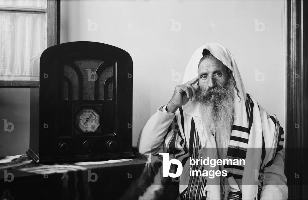 Yemenite Rabbi, in traditional robes and prayer shawl, listening to radio, c. 1937