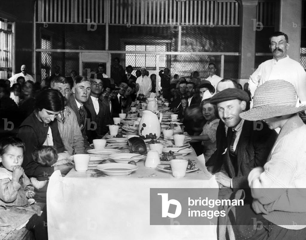Immigrants who are awaiting approval of their entry into the U.S. crowd in the lunchroom for their noonday meal. Ellis Island, New York. c. 1923