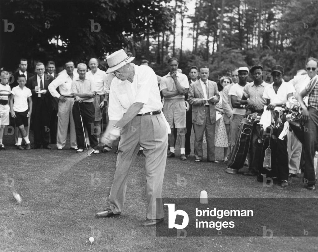 President Dwight Eisenhower teeing off. His audience includes African American caddies. August 1957.