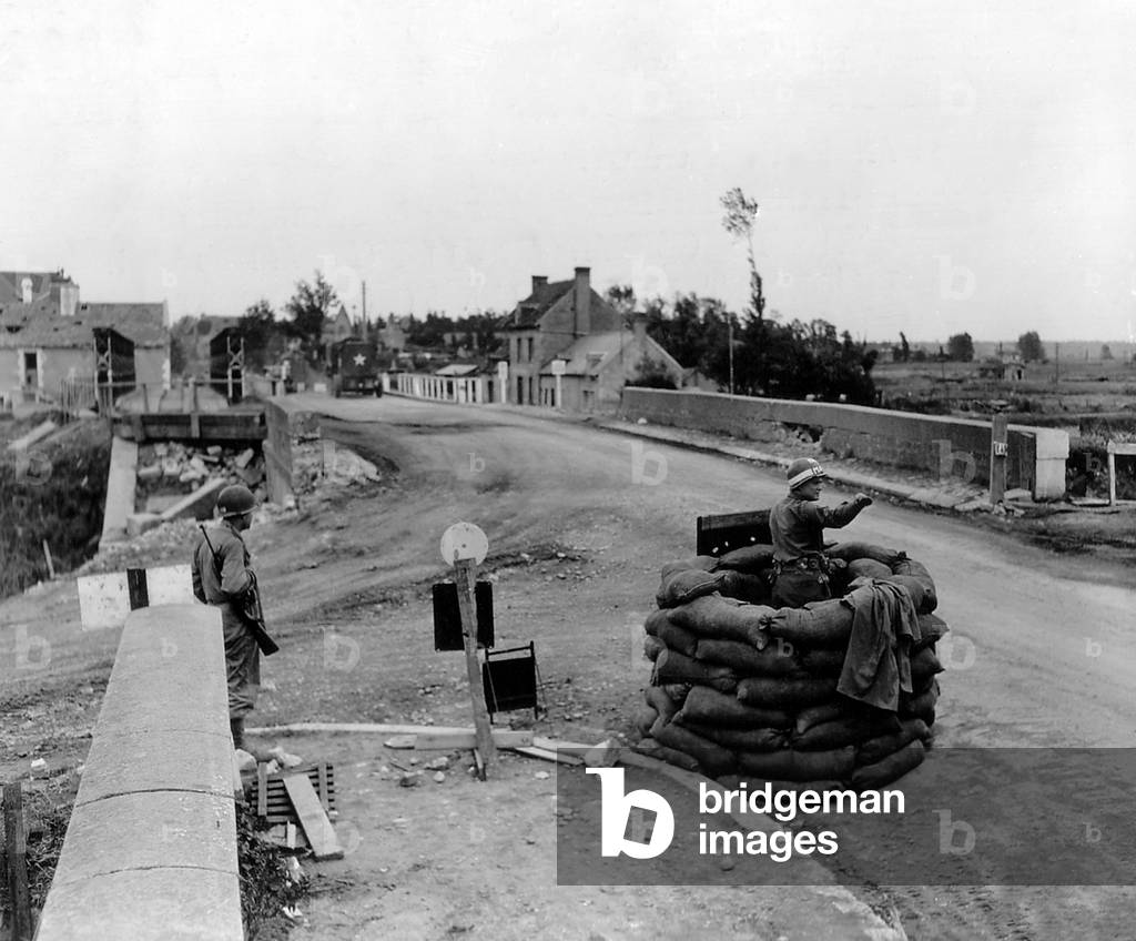U.S. MP controls traffic on a bridge at Carentan, sheltered in a 'booth' made ??with sandbags. July 5, 1944. Normandy Campaign, France, World War 2