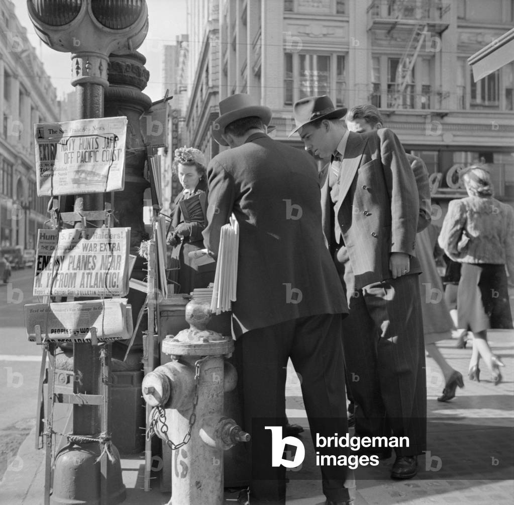 Newspaper stand on Monday morning, Dec. 8, 1941, the day after Japanese attack on Pearl Harbor. Headline reads, 'ENEMY PLANES NEAR N.Y. FROM ATLANTIC. Montgomery and Market Streets, San Francisco, California