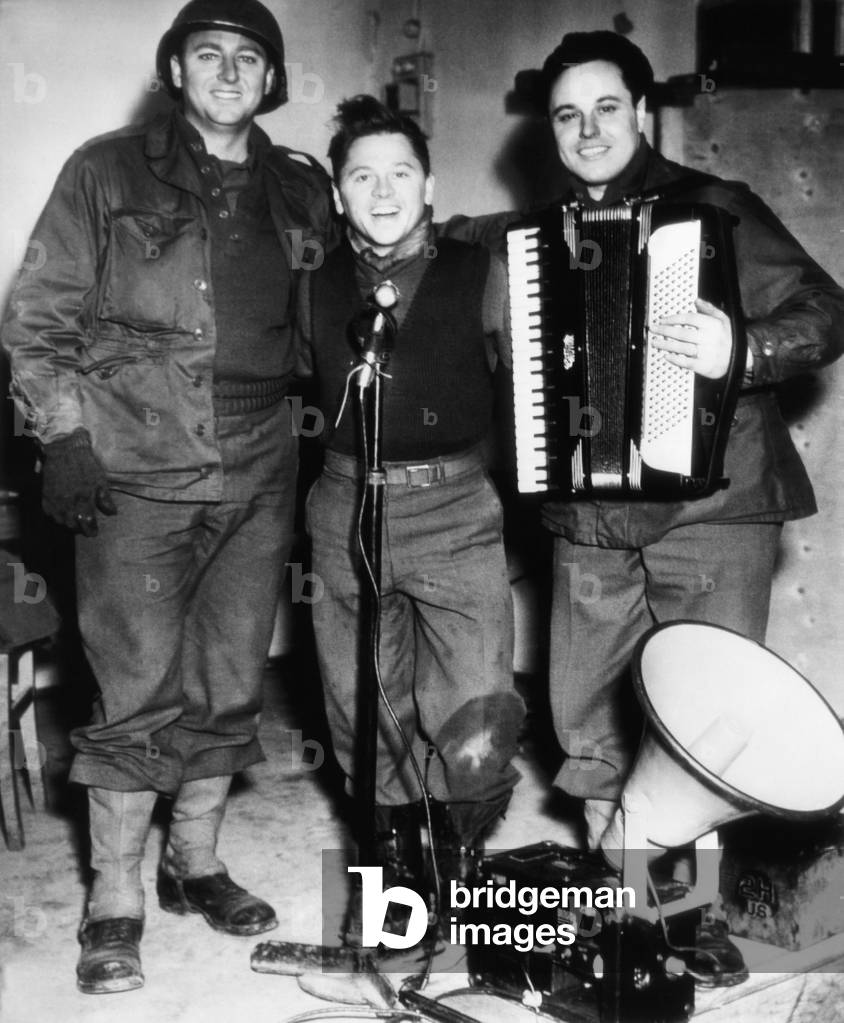 Mickey Rooney (center), entertains troops of the 26th division in Europe, at left is Private Mario Pierone, right, Private Bob Priester, January 17, 1945