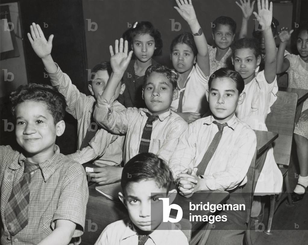 Puerto Rican children in a classroom, some with hands raised. New York City, April 25, 1947