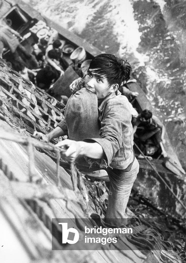 Vietnam War, South China Sea, a Vietnamese Refugee with his belongings secured in between his teeth, climbs a cargo net to the deck of the combat store ship USS White Plains, AFS-M. The ship is picking up twenty-nine refugees from a 35 Foot wooden Boat, July 30, 1979