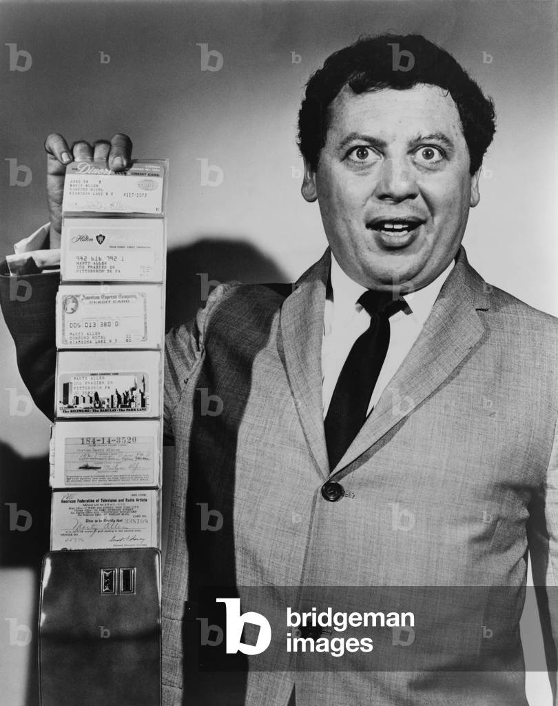 Comedian Marty Allen, holding wallet with four credit cards. Consumer credits cards, introduced in the 1950's, became common in the 1960's. 1960