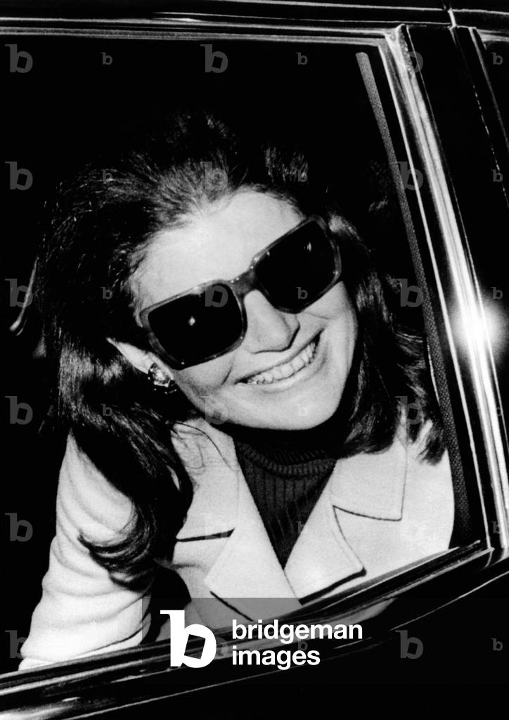 Jacqueline Kennedy Onassis smiles as she talks with newsman upon arrival at Logan International Airport, 1970 (b/w photo)