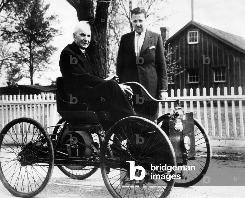 Henry Ford sits in his first Ford car built in 1896, as his grandson, Henry Ford II stands nearby. c. 1946