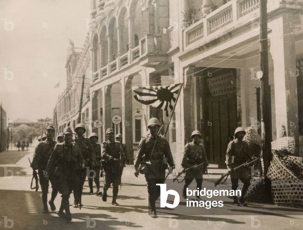 Japanese troops march in the streets of Hainan Island with a Rising Sun flag. May 3, 1939. Chinese Communists and the Hainan Li natives fought against the Japanese occupation and over one third of the male population were killed by the Japanese.