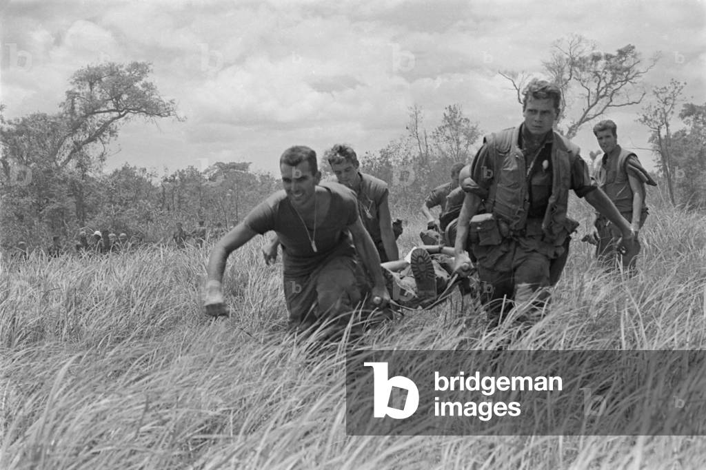 Vietnam War. While under heavy fire, US Marines are carry a wounded Marine to the evacuation helicopter near the Demilitarized Zone (DMZ) dividing North and South Vietnam. July 7, 1967