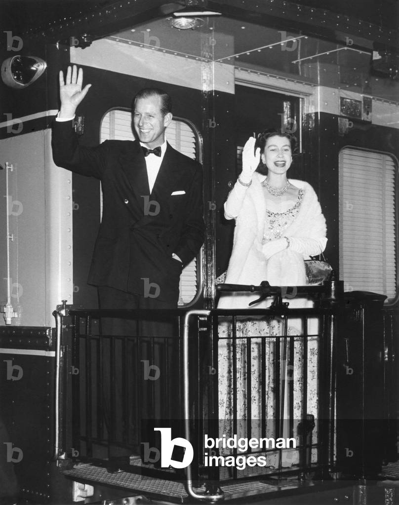 Queen Elizabeth II and Prince Philip wave from the back of a train at Union Station. After entertaining the President Eisenhower and the First Lady, they leave for New York City. Oct. 20, 1957 (b/w photo)