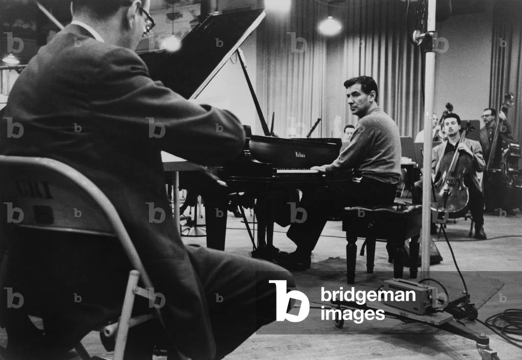 Leonard Bernstein, playing piano, amidst other musicians during a rehearsal in 1958