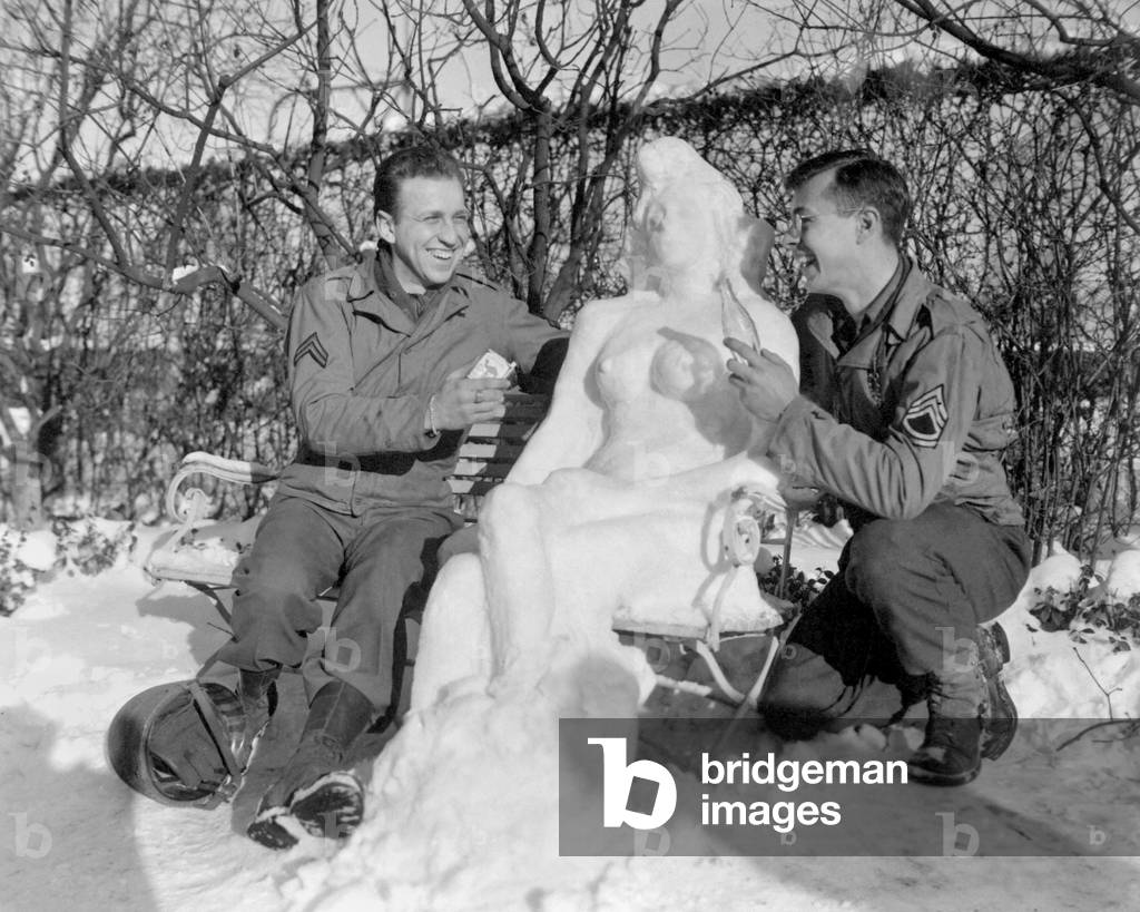Two U.S. soldiers offer 'Agnes' their snow woman, Camel cigarettes and a Coke. European theater. Jan. 14, 1945. World War 2