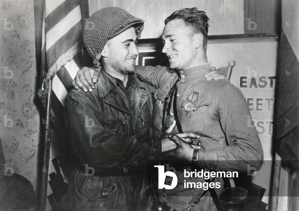U.S. Lt. William Robertson and Soviet Lt. Alexander Sylvashko embrace. Behind them is a sign, 'East Meets West' to celebrate the meeting of the Soviet (Russian) and American armies, near Torgau, Germany. April 25, 1945. World War 2
