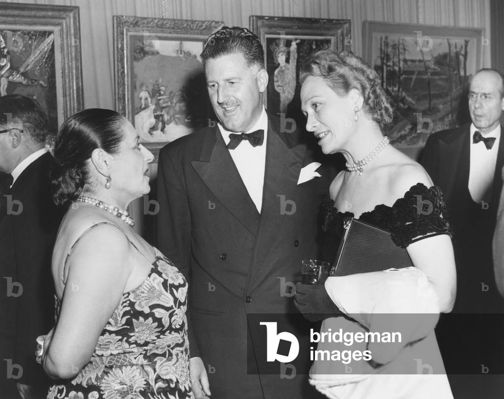 Helena Rubenstein, world famous cosmetician and art collector greets guests at her NYC home. Oct. 1950. She was opening her new penthouse art galleries, displaying her collections of modern and surrealist art. Rubenstein talks with Paul Williams and Mrs. Dee Bredanat a benefit for the Hospitalized Veterans Music Service