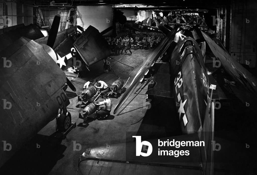 Surrounded by F6F Hellcat fighters, seamen prepare bombs on hangar deck of USS Yorktown. c. 1943. World War 2, Pacific Ocean